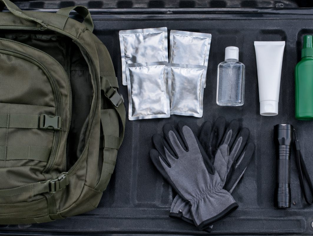 Responder go-bag laid out on a tailgate with foil packs, sanitizer, sunscreen, repellent, gloves and a flashlight