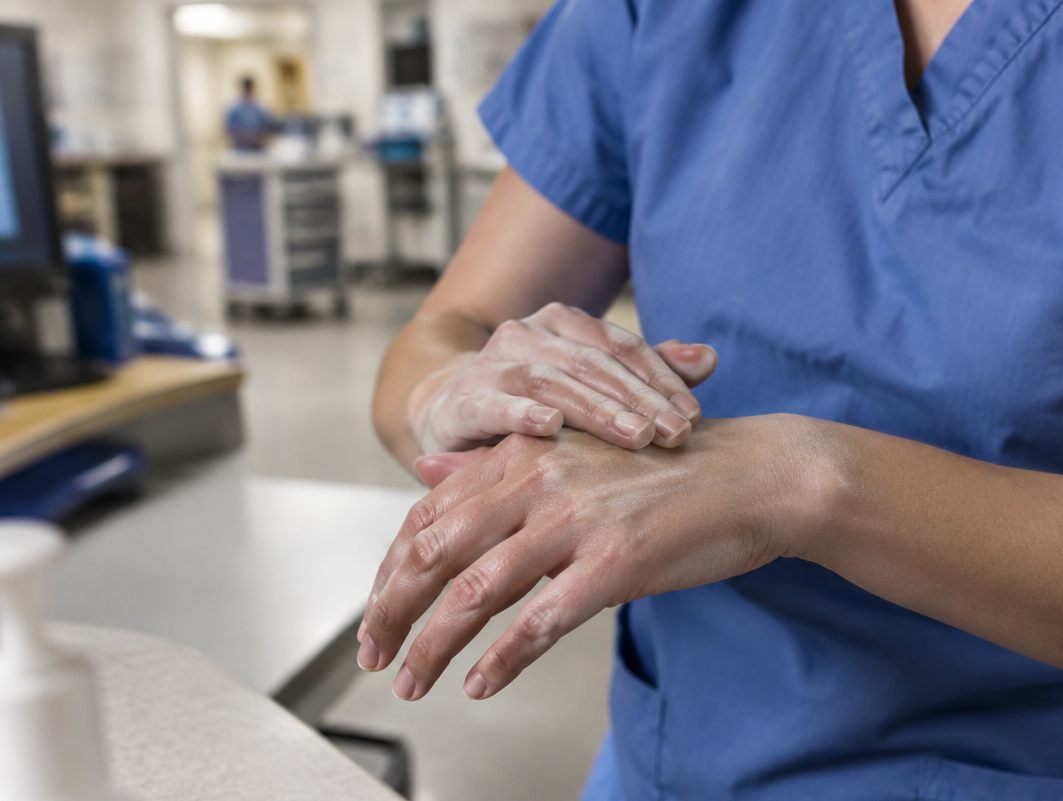 Nurse in scrubs working lotion into her hands at the nurses' station